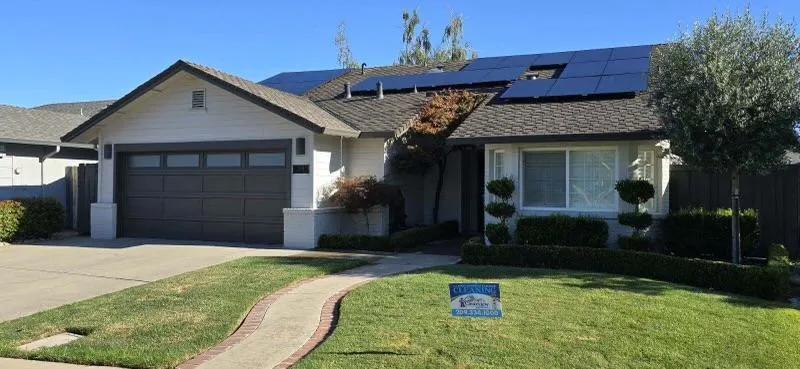 Single-story house with a garage, solar panels, and manicured lawn.